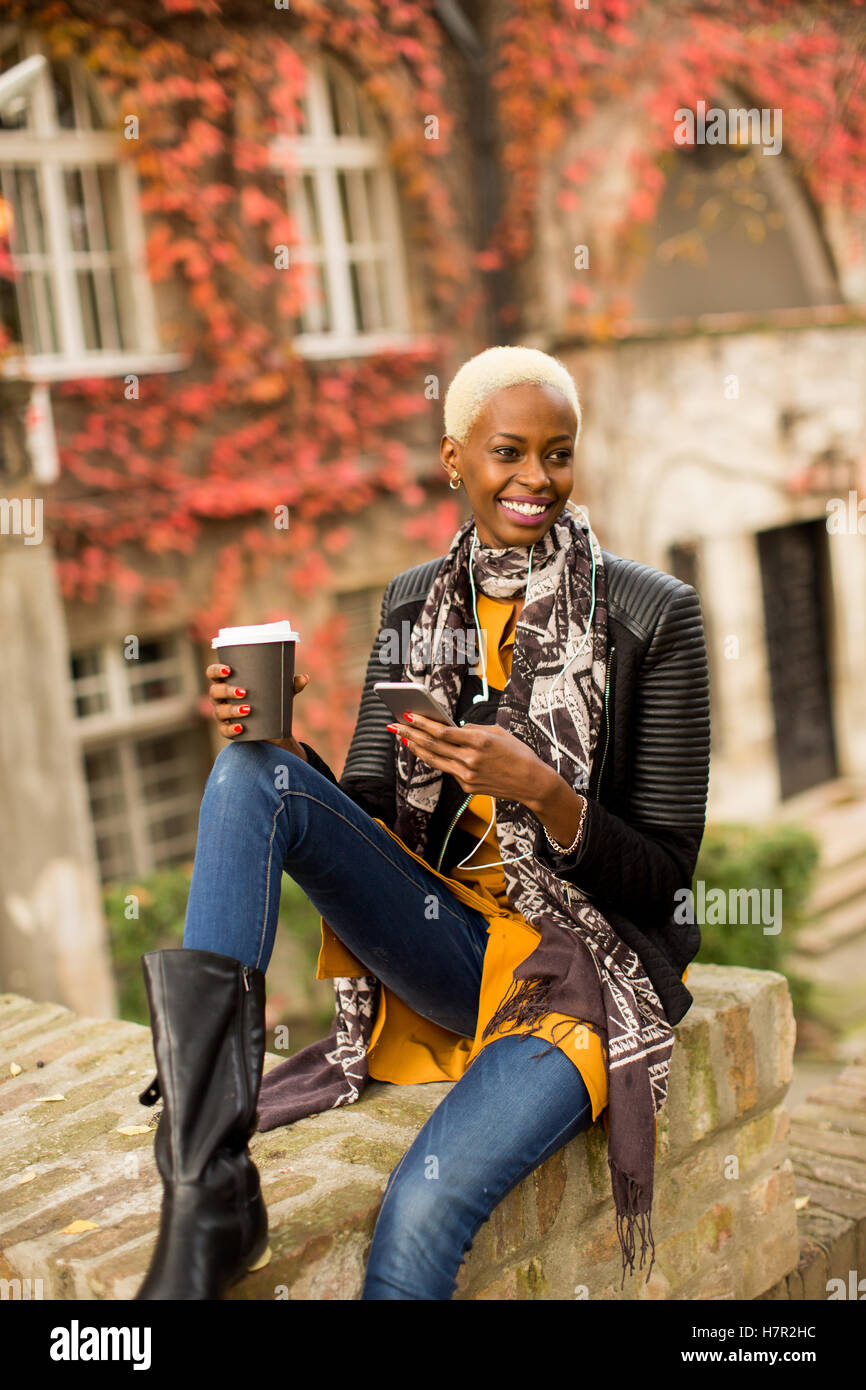 Moderno e giovane africano donna americana in posa con caffè di andare e il telefono cellulare all'aperto Foto Stock