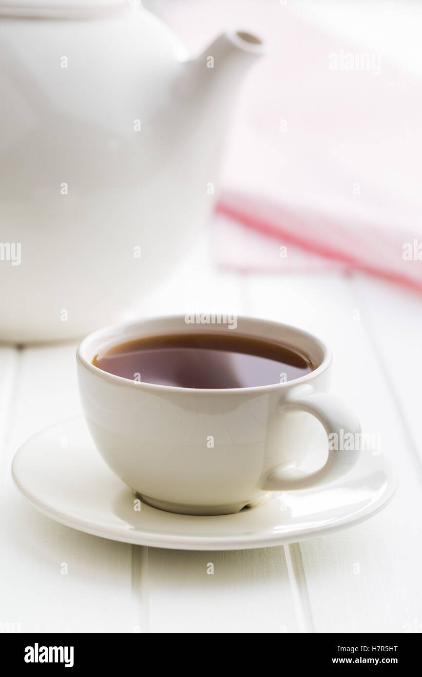 Una tazza di tè nero e teiera sul tavolo bianco. Foto Stock