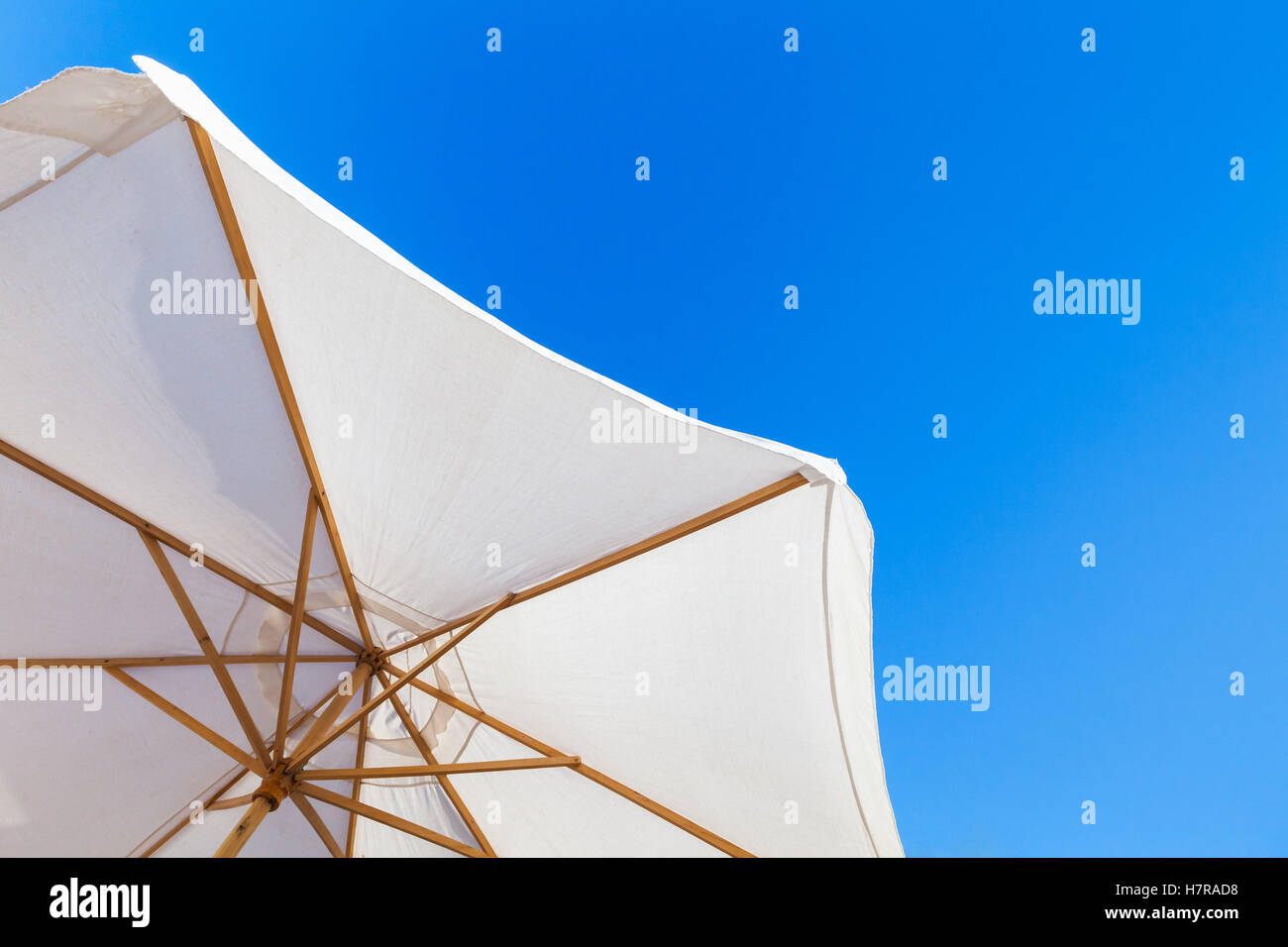 Bianco ombrello aperto sotto il luminoso cielo blu in giornata estiva, resort foto di sfondo Foto Stock