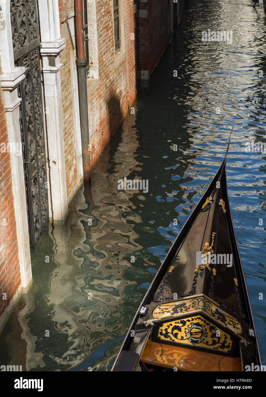 Prua di una gondola in un canale accanto a un muro di mattoni; Venezia, Italia Foto Stock