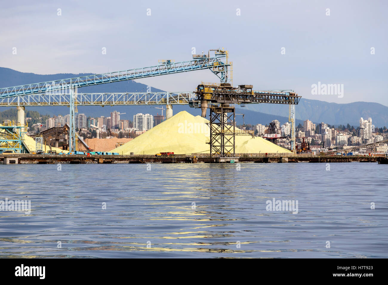 Pile di zolfo si trovano sotto le gru e nastri trasportatori in Un cantiere navale di Vancouver, porto di Vancouver in attesa di carico e trasporto per ex... Foto Stock