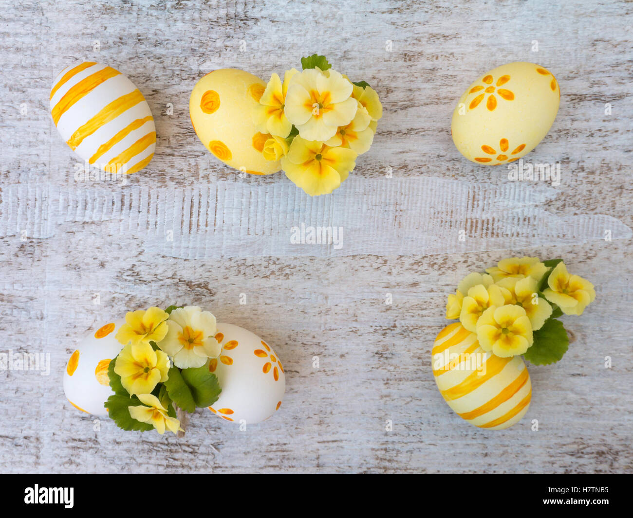 Il bianco e il giallo delle uova di Pasqua decorate da strisce, punti e fiori e primrose sul bianco tavola di legno Foto Stock