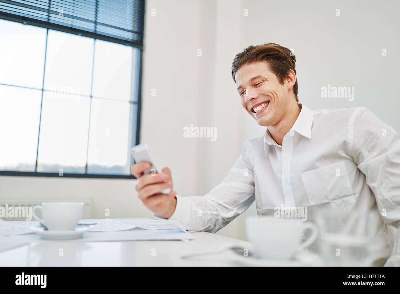 Imprenditore sorridente con lo smartphone legge SMS con gioia Foto Stock