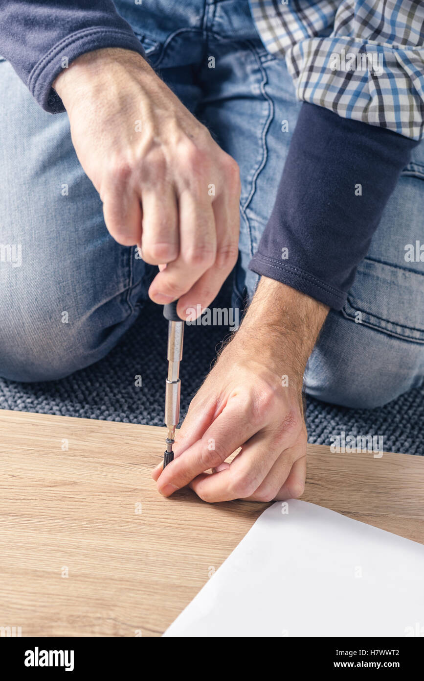 L'uomo assemblaggio di mobili a casa sul pavimento, a mano con un cacciavite Foto Stock