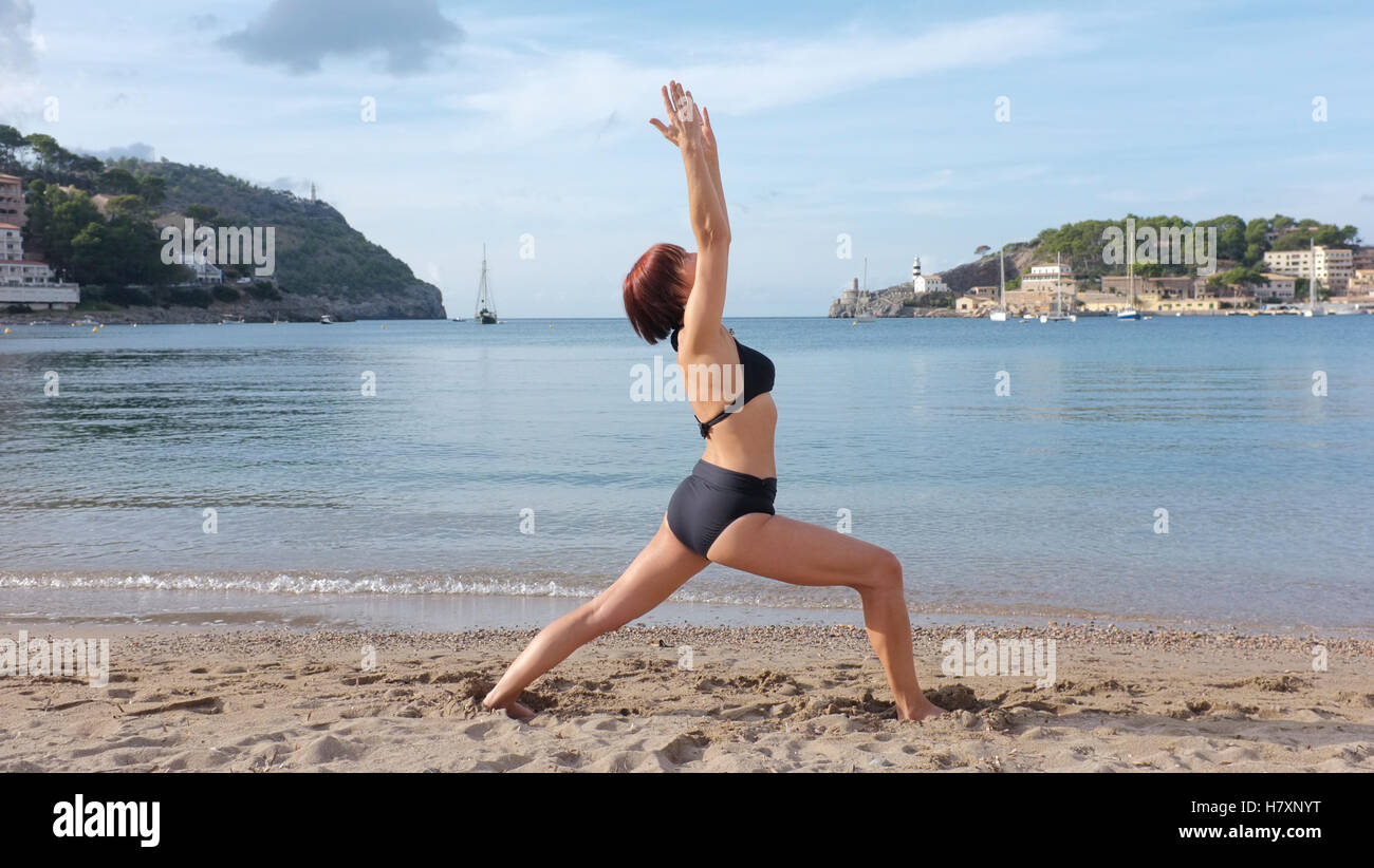Una donna a praticare yoga su una spiaggia in Maiorca. guerriero 1 pongono mostrato. Foto Stock
