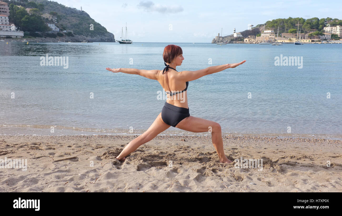 Una donna a praticare yoga su una spiaggia in Maiorca. guerriero pongono mostrato. Foto Stock