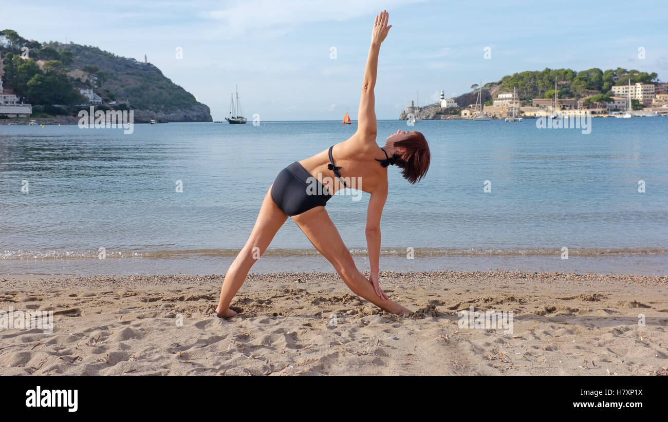 Una donna a praticare yoga su una spiaggia in Maiorca. triangolo pongono mostrato. Foto Stock