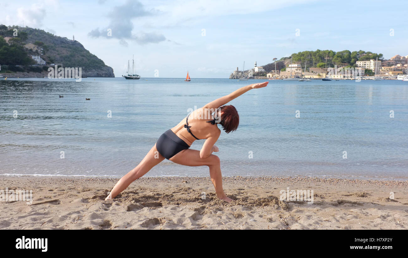 Una donna a praticare yoga su una spiaggia in Maiorca. laterale ad angolo pongono mostrato. Foto Stock