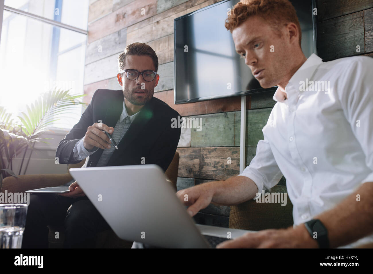 Due giovani uomo seduto in ufficio e discutere di affari con computer portatile. Colleghi di lavoro che lavora sul computer portatile durante la riunione. Foto Stock