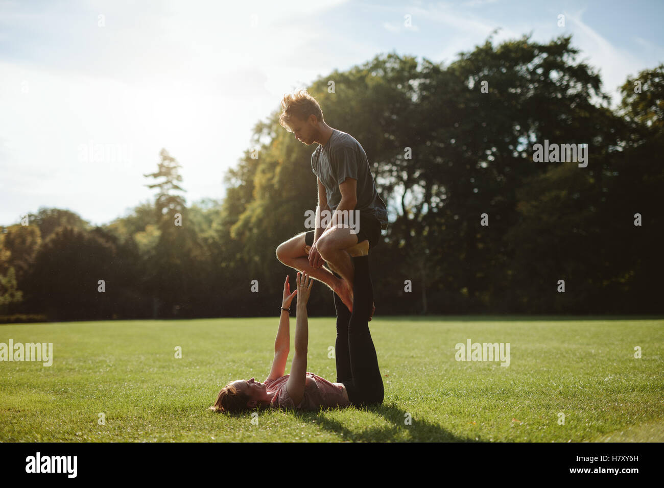 Flessibile e forte coppia giovane facendo acroyoga all'esterno. L uomo e la donna nel parco coppia pratica yoga pone. Foto Stock