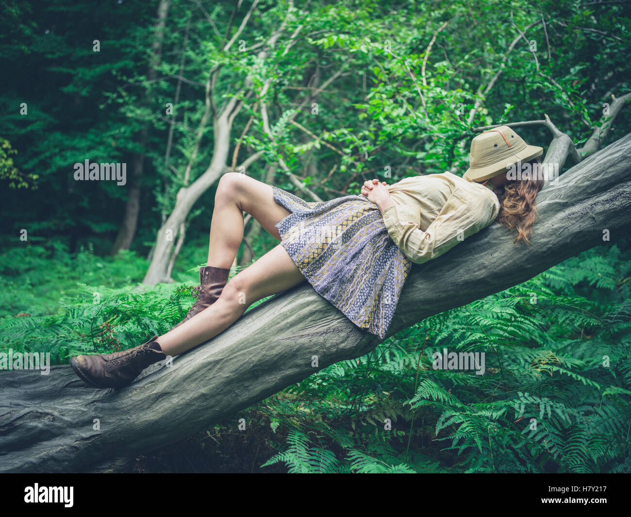 Una giovane donna è sdraiato su un albero caduto nella foresta circondato da felci con un safari hat che copre il volto Foto Stock