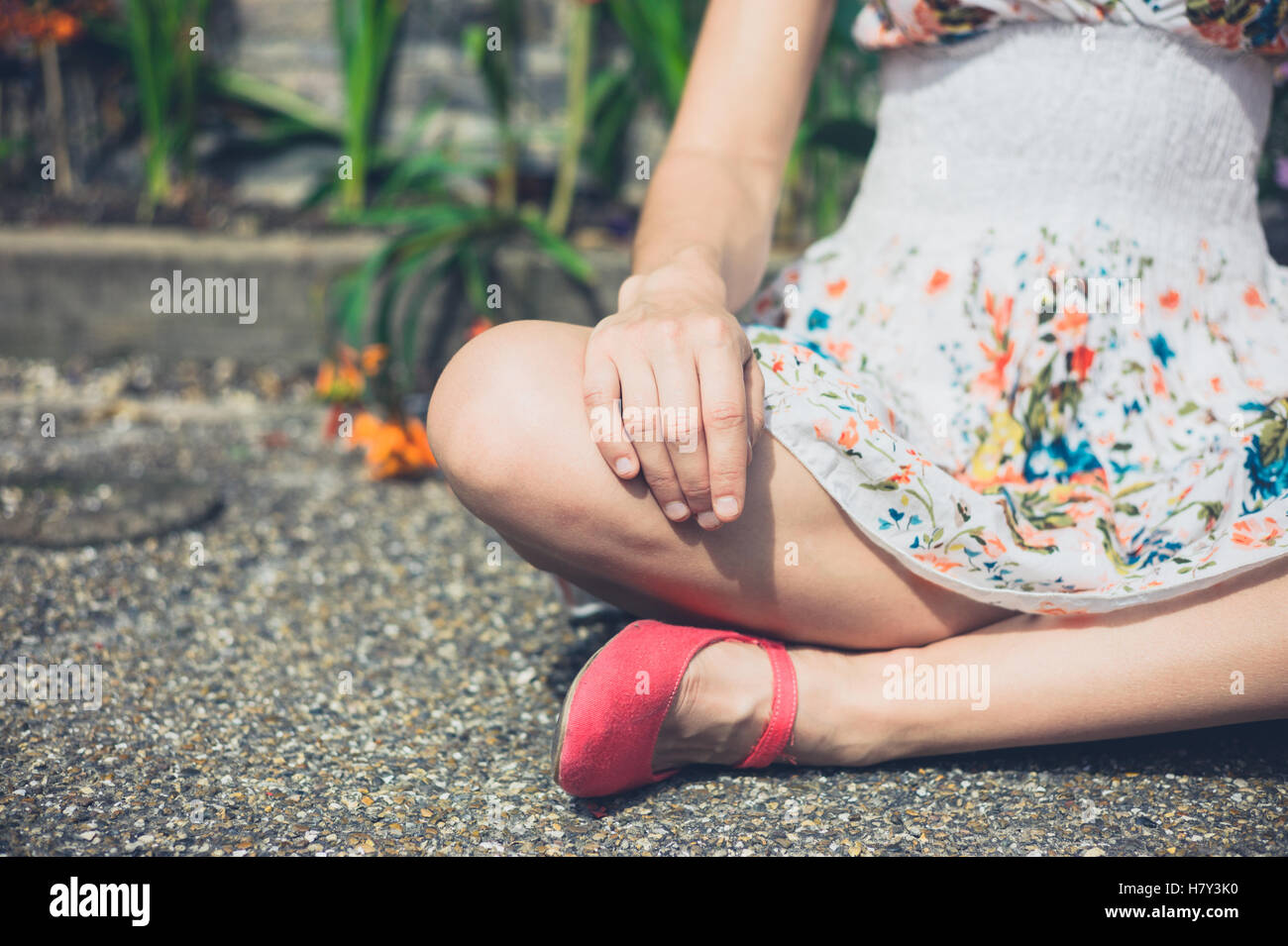 Una giovane donna è seduta in una meditazione pongono al di fuori sul terreno da alcuni fiori Foto Stock