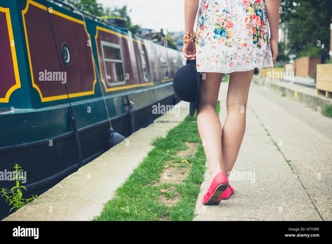 Una giovane donna è a piedi lungo il canale in una giornata di sole in estate e sta passando una casa galleggiante Foto Stock
