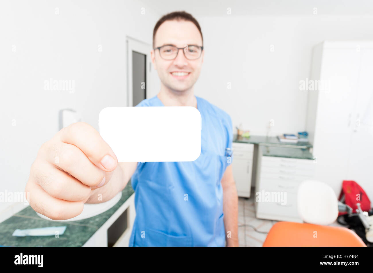 Felice bello dentista mostra business card in piedi è il suo gabinetto Foto Stock