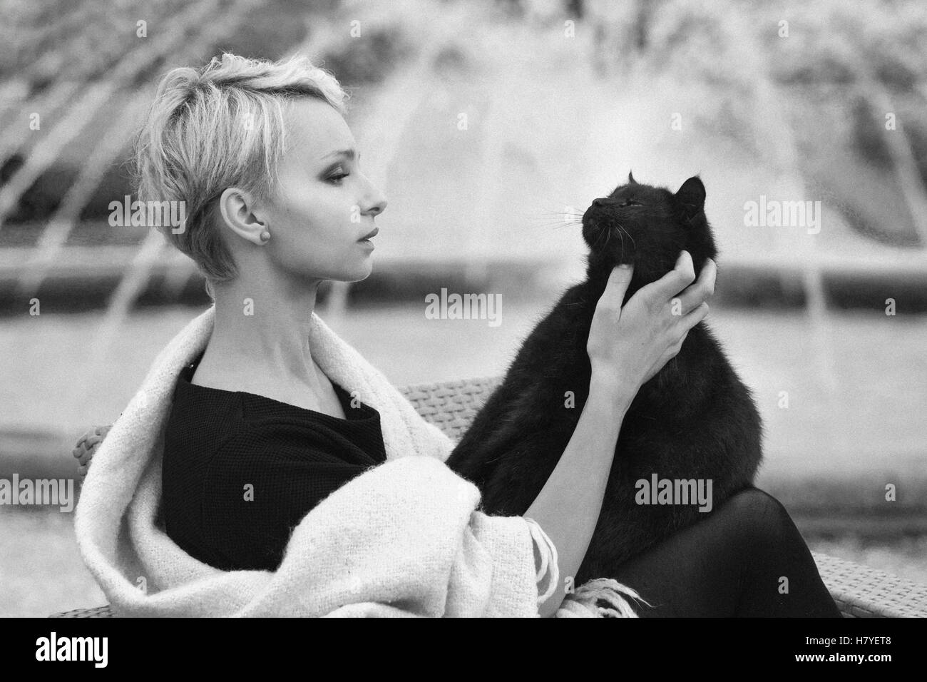 Una bella donna bionda con un gatto nero, tenendo un gatto nero, accarezzare un gatto Foto Stock