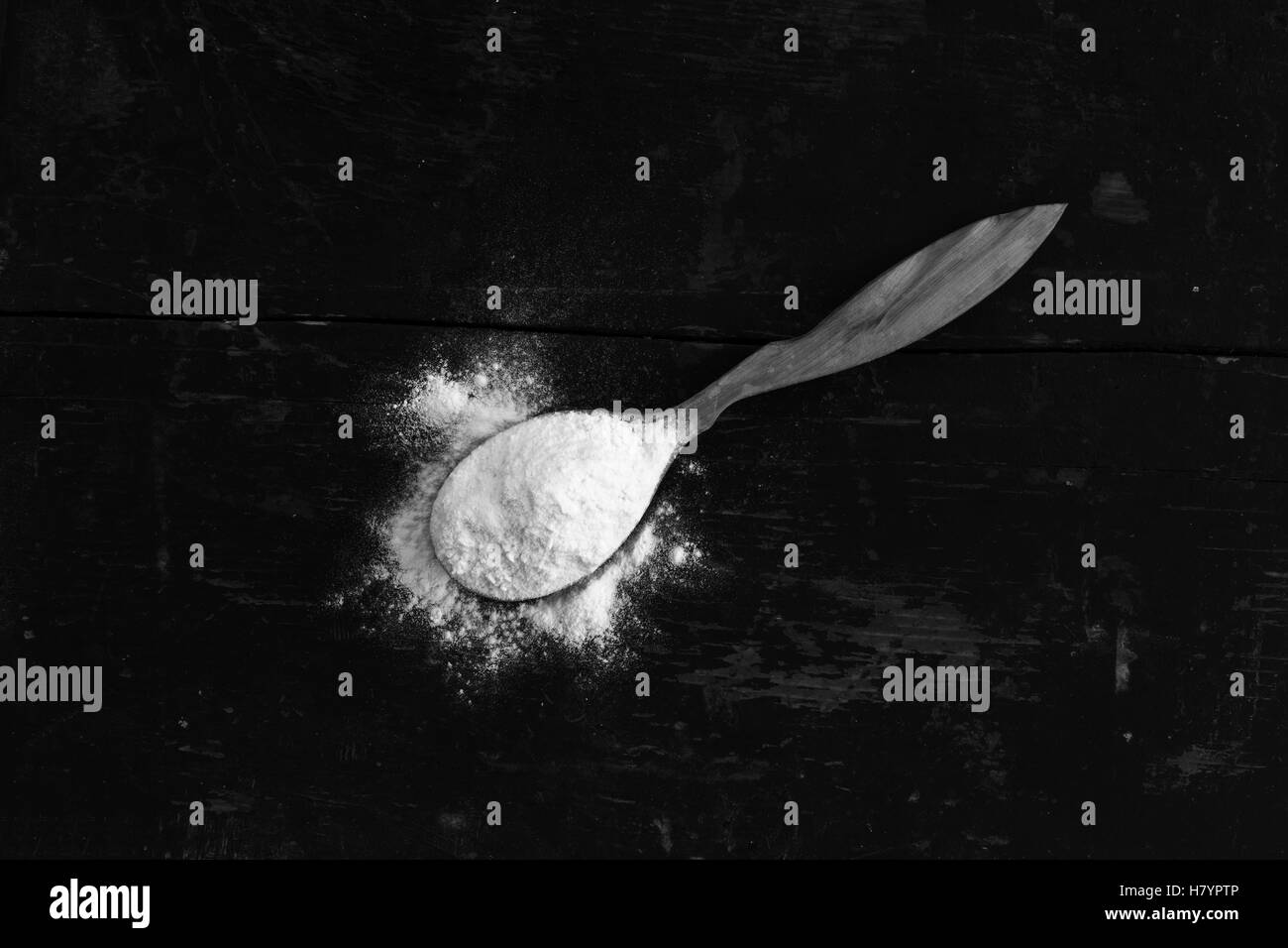 La farina di frumento bianca in un cucchiaio di legno sul vecchio incrinato bancone. foto in bianco e nero Foto Stock