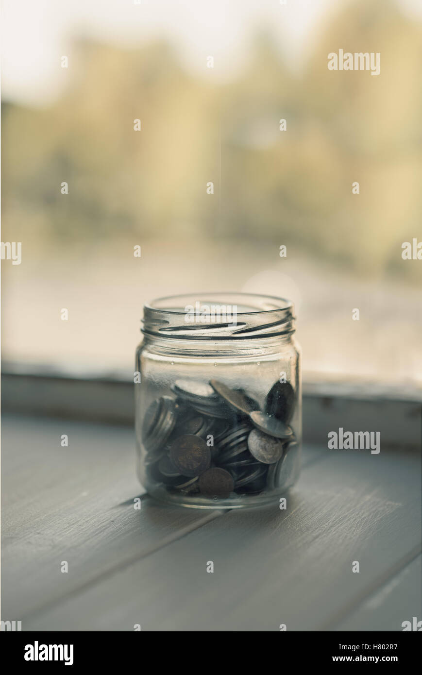 Vaso di vetro con vecchie monete accanto a una finestra. vintage elaborati. spazio copia Foto Stock