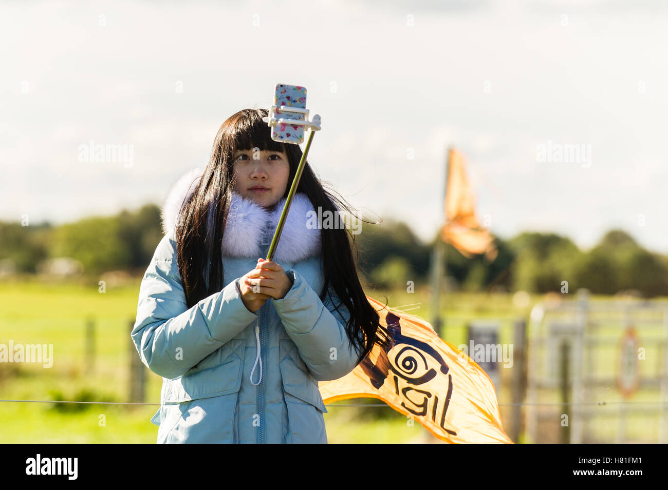 Giovane donna prende un selfie utilizzando un mobile/smart phone e un bastone selfie. Foto Stock