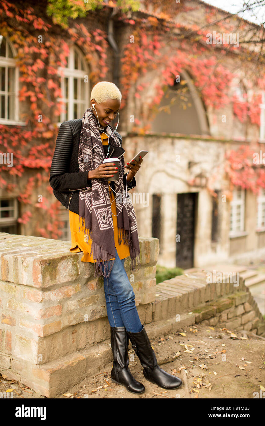 Moderno e giovane africano donna americana in posa con caffè di andare e il telefono cellulare all'aperto Foto Stock