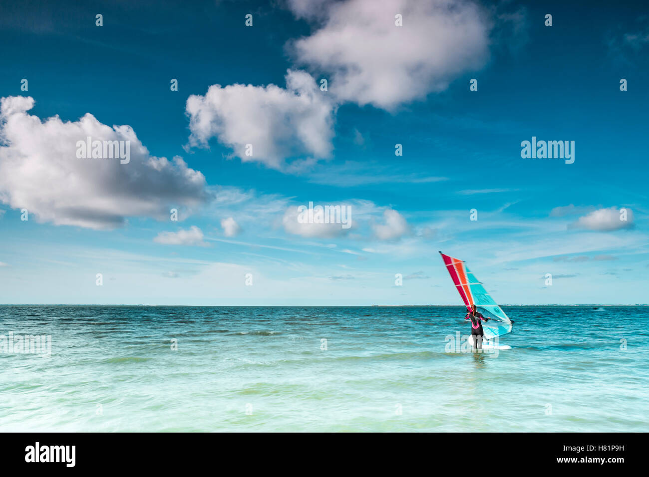 Surfista del vento sul suo bordo su un oceano tranquillo sul mare del Nord su un soleggiato blue sky giornata con nubi in un ambiente marino o nautiche il viaggio Foto Stock