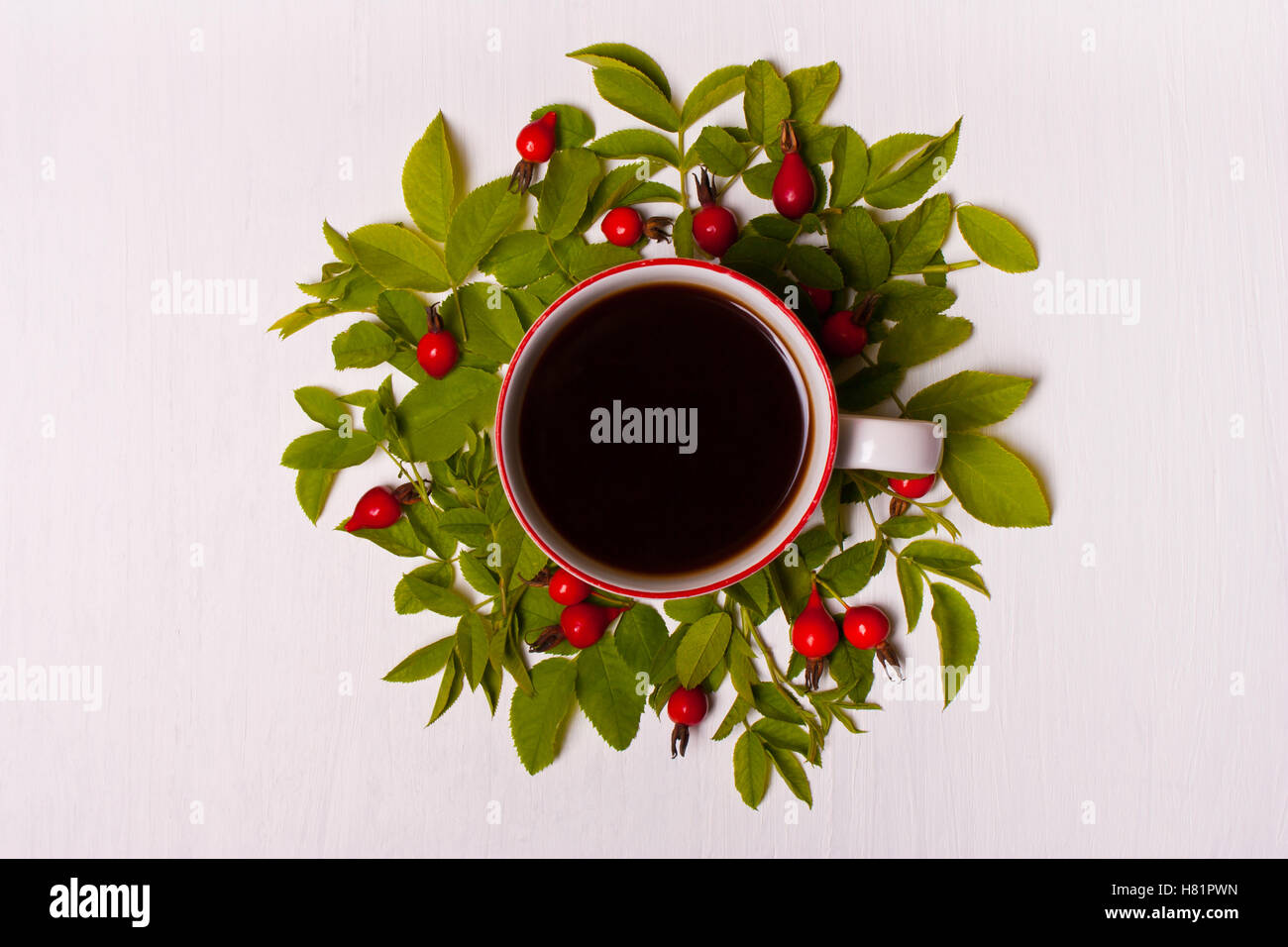 Tazza di caffè su sfondo bianco in foglie verdi e rosse bacche, fiori.Flat laico, vista dall'alto Foto Stock
