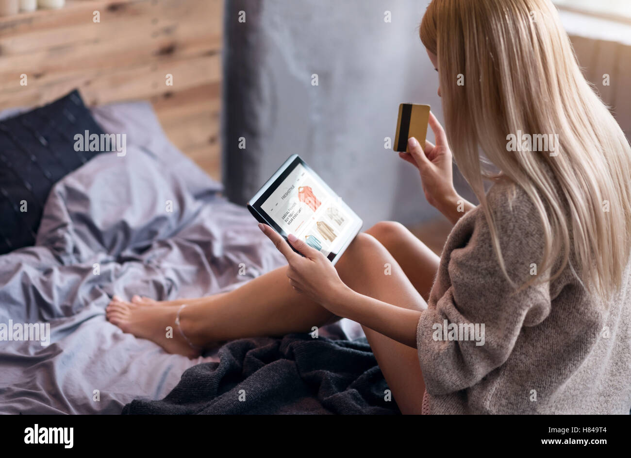 Giovane donna avente lo shopping online in camera da letto Foto Stock