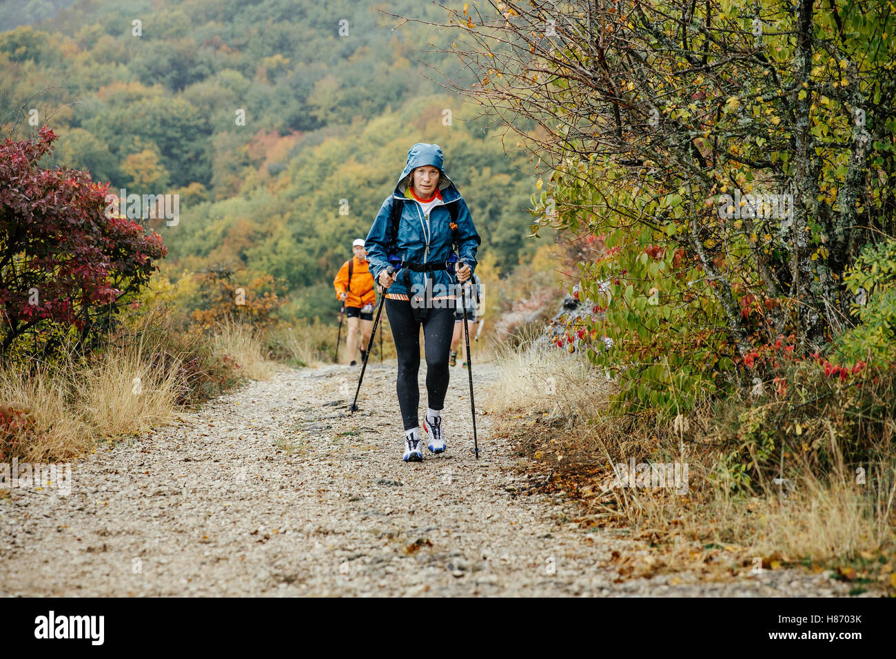 Donna di mezza età con bastoncini che viaggiano in condizioni di tempo piovoso sul sentiero di montagna Foto Stock