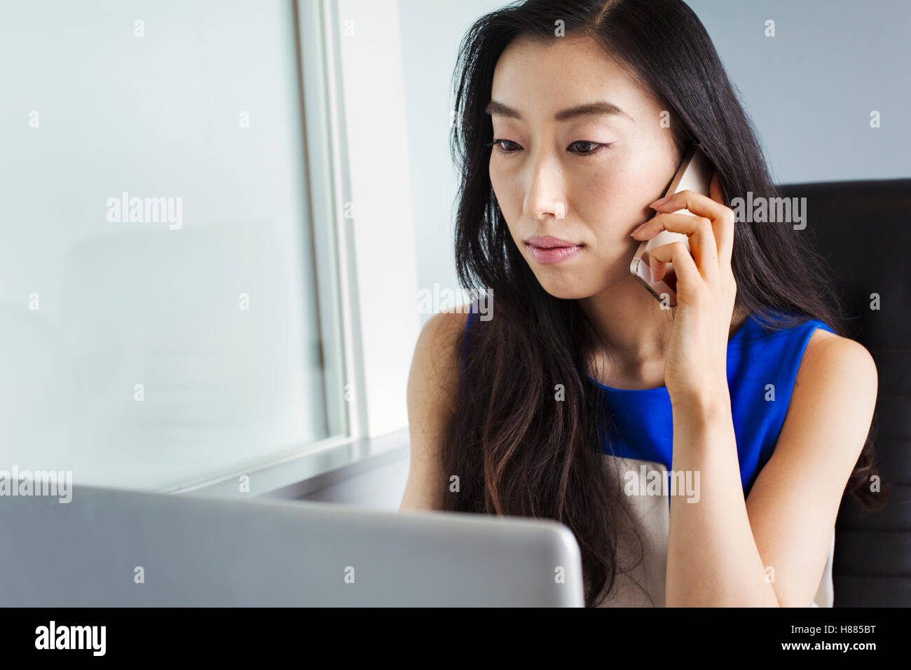 Una donna d'affari in preparazione per il lavoro, seduta usando il suo computer portatile e parlando su il suo smart phone. Foto Stock