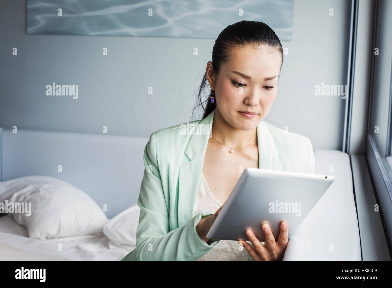 Una donna d'affari in preparazione per il lavoro, seduto su un letto utilizzando una tavoletta digitale. Foto Stock