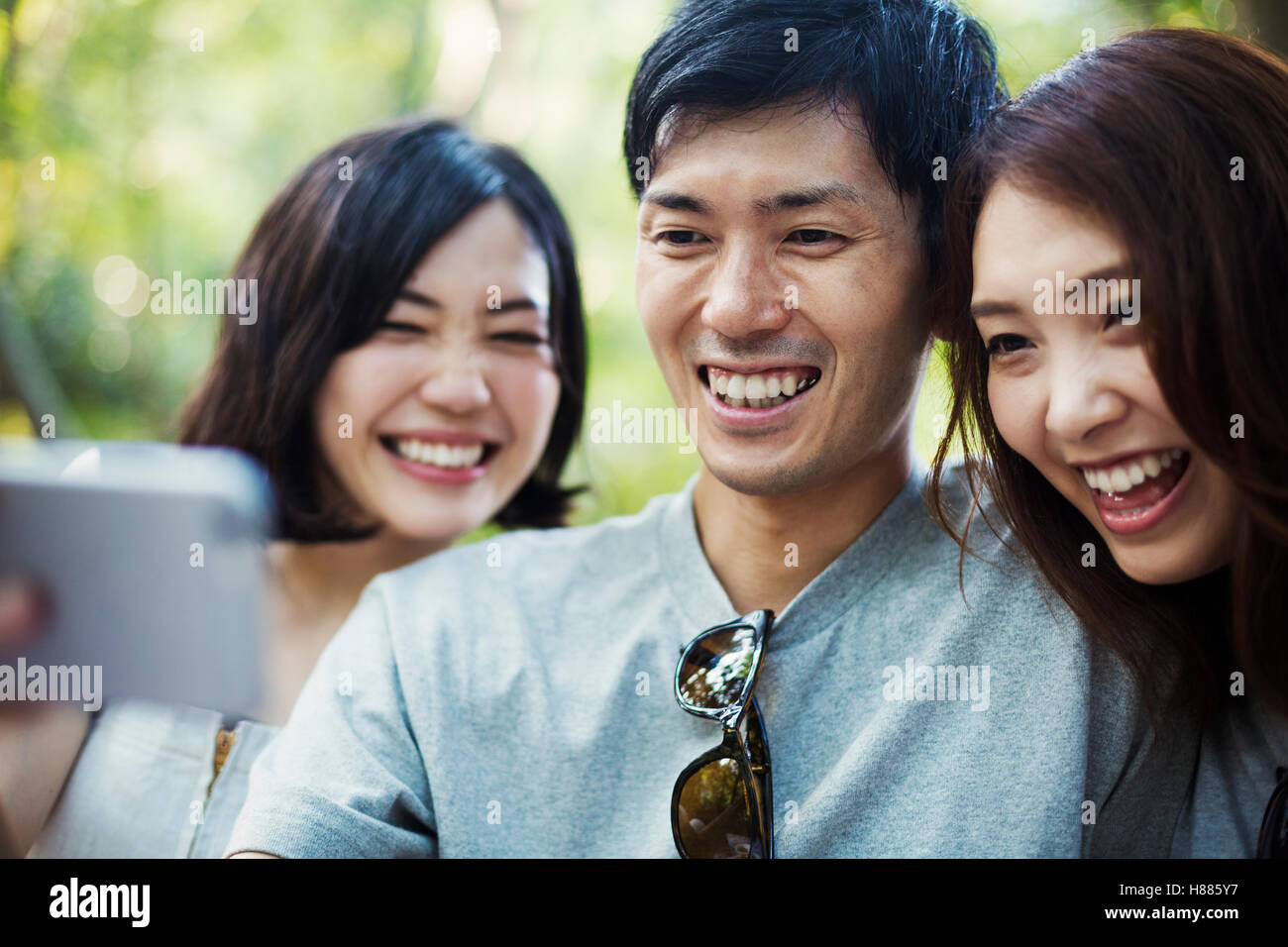 Due giovani donne e un uomo seduto in una foresta, prendendo un selfie. Foto Stock