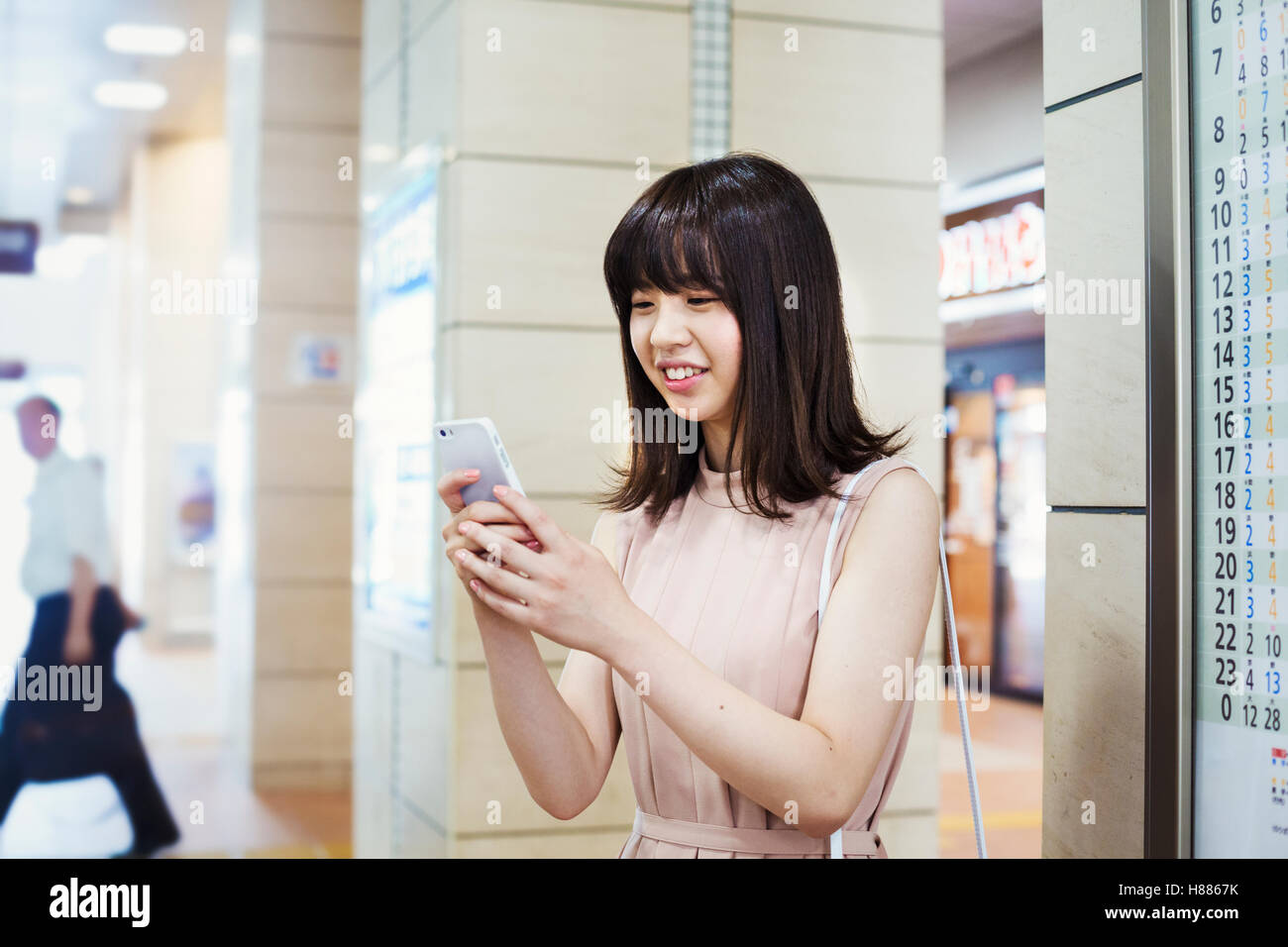 Sorridente giovane donna con capelli lunghi marrone, tenendo in mano un telefono cellulare. Foto Stock