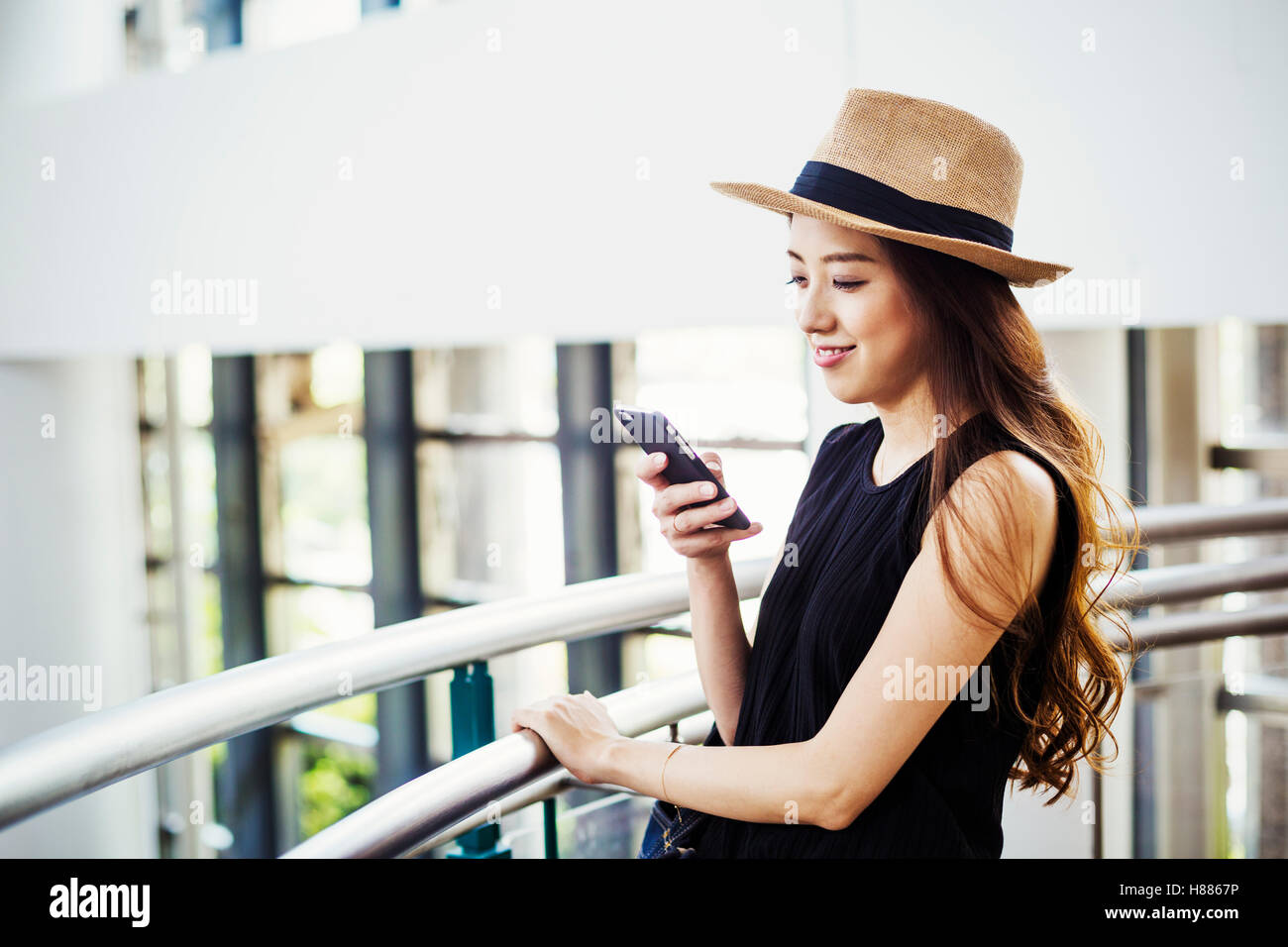 Giovane donna con capelli lunghi marrone, indossando un cappello di Panama, in un centro commerciale, utilizzando un telefono cellulare. Foto Stock