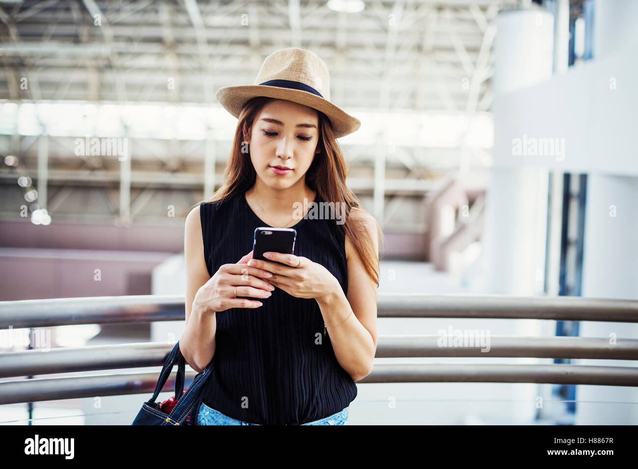 Giovane donna con capelli lunghi marrone, indossando un cappello di Panama, in un centro commerciale, utilizzando un telefono cellulare. Foto Stock
