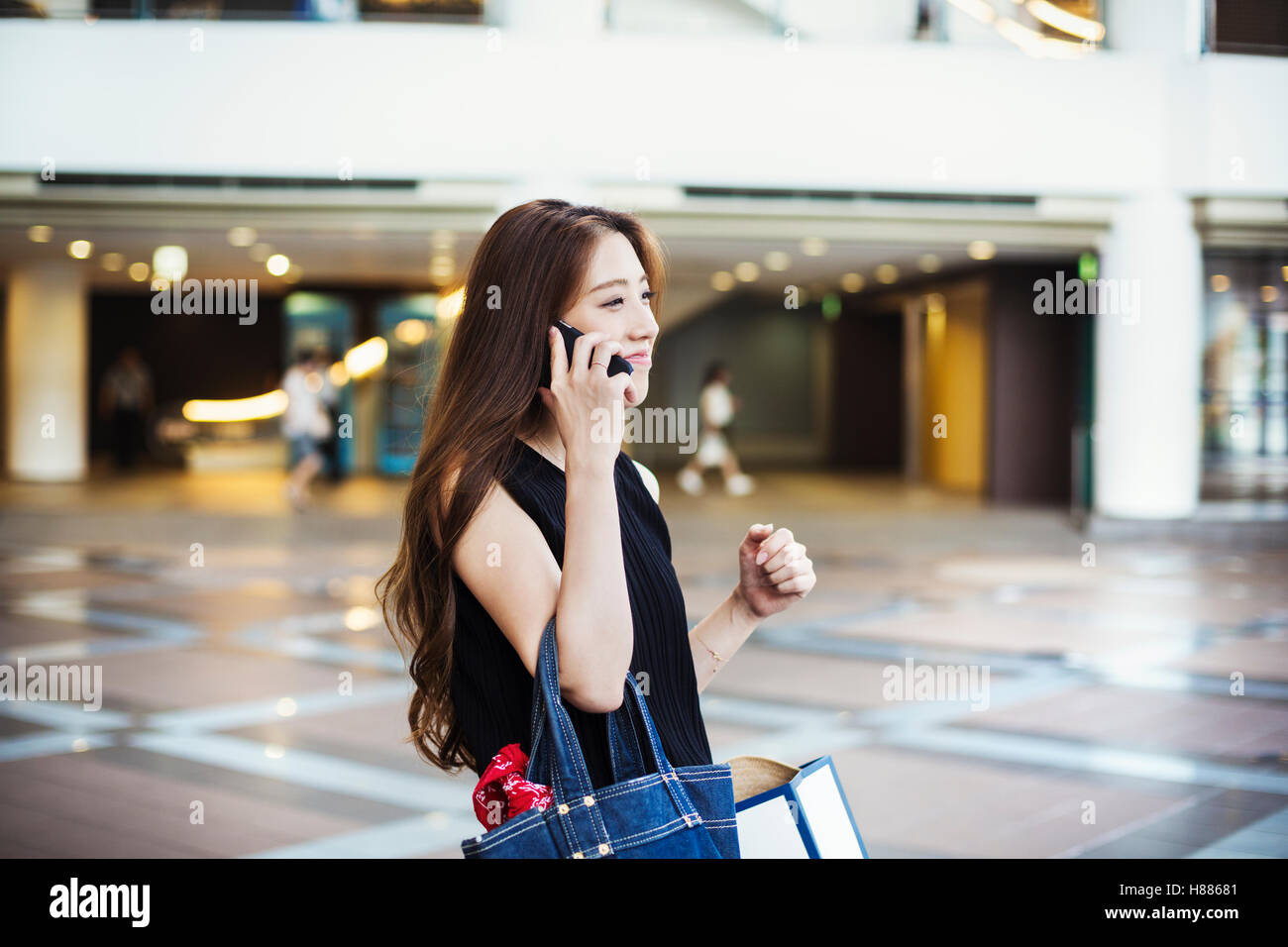 Giovane donna con capelli lunghi marrone in un centro commerciale, sul telefono. Foto Stock