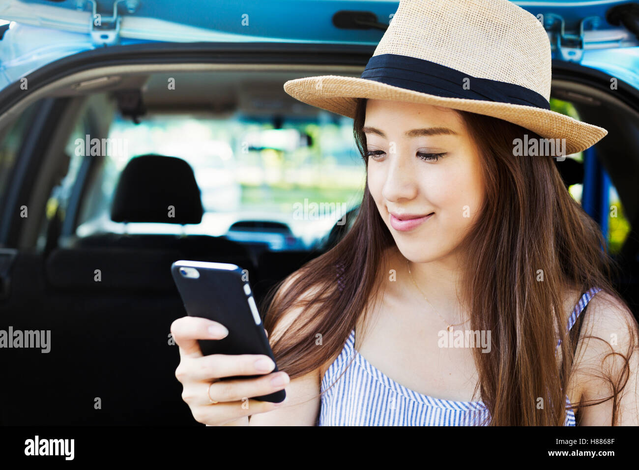 Sorridente giovane donna con capelli lunghi marrone, indossare un cappello di Panama, utilizzando un telefono cellulare. Foto Stock
