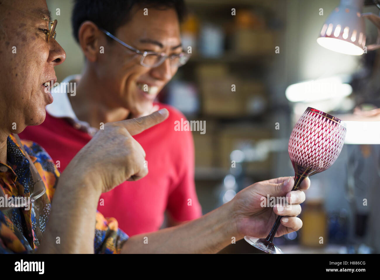 Due persone, padre e figlio al lavoro in un vetro maker's studio workshop, ispezione di un taglio rosso vino in vetro Vetro. Foto Stock