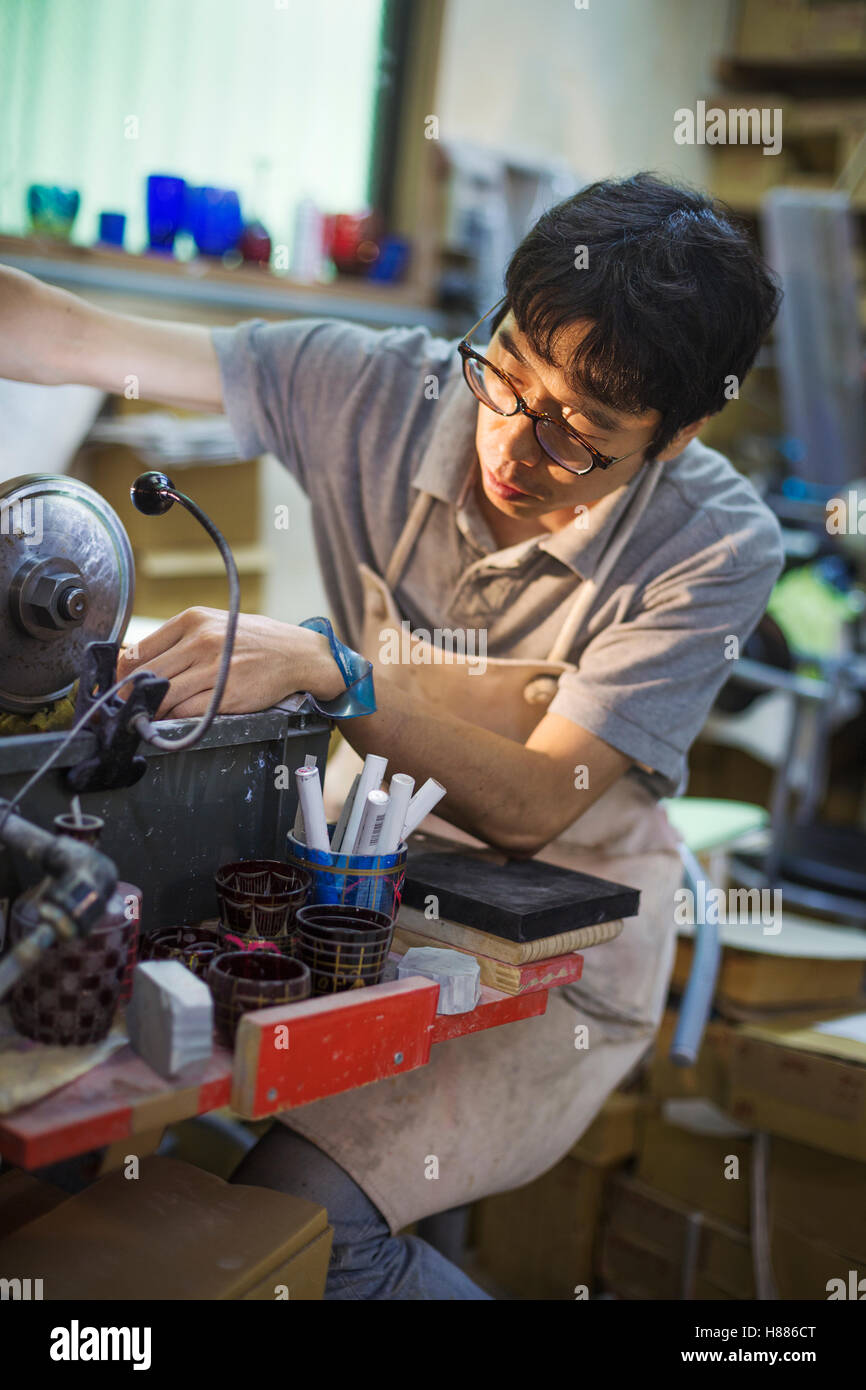 Un artigiano al lavoro in un vetro maker's workshop, utilizzando una macchina per attacco in vetro. Foto Stock