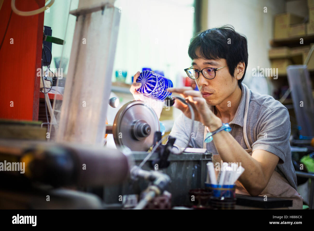 Un artigiano al lavoro in un produttore di vetro del workshop la lucidatura di un azzurro intenso cut oggetto in vetro. Foto Stock