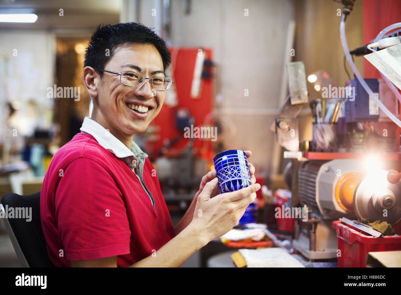 Un artigiano al lavoro in un vetro maker's workshop lavorando su un blu vivo tagliare oggetto in vetro. Foto Stock