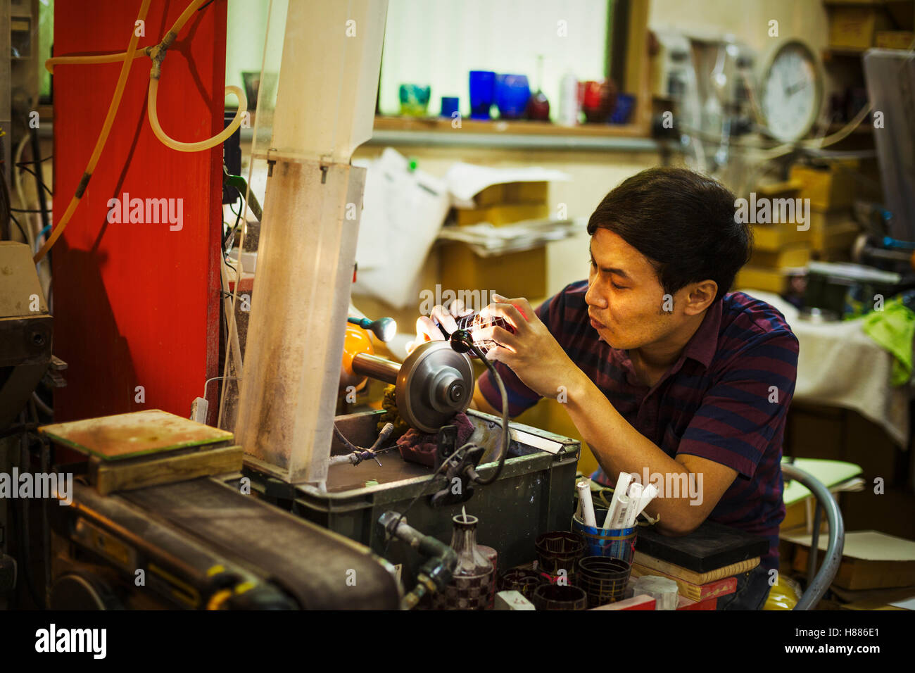 Un artigiano al lavoro seduta utilizzando una macchina di molatura per etch e contrassegnare un pattern su un oggetto in vetro. Foto Stock