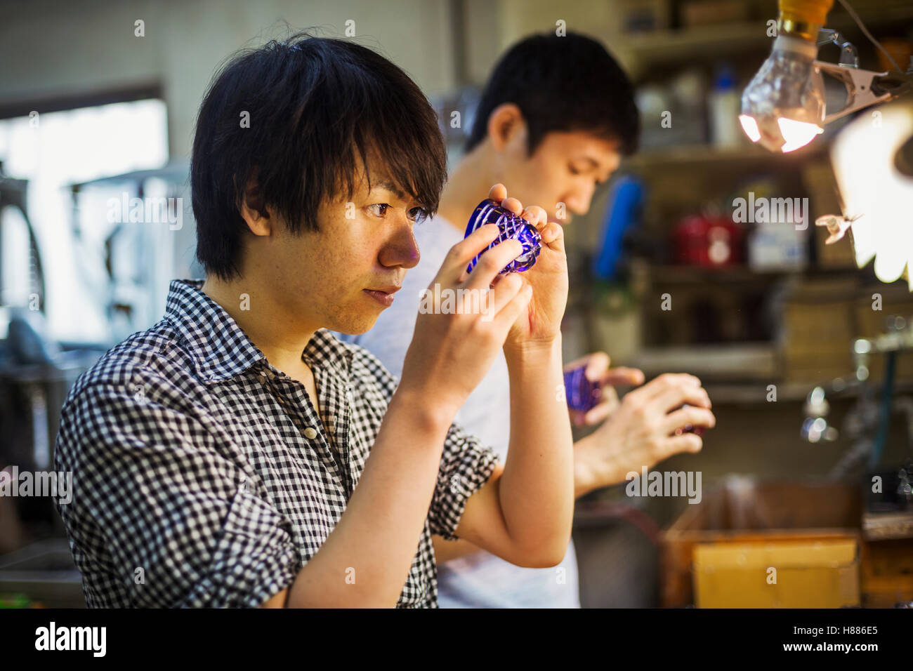 Un artigiano al lavoro in un vetro maker's workshop lavorando su un blu vivo tagliare oggetto in vetro. Foto Stock