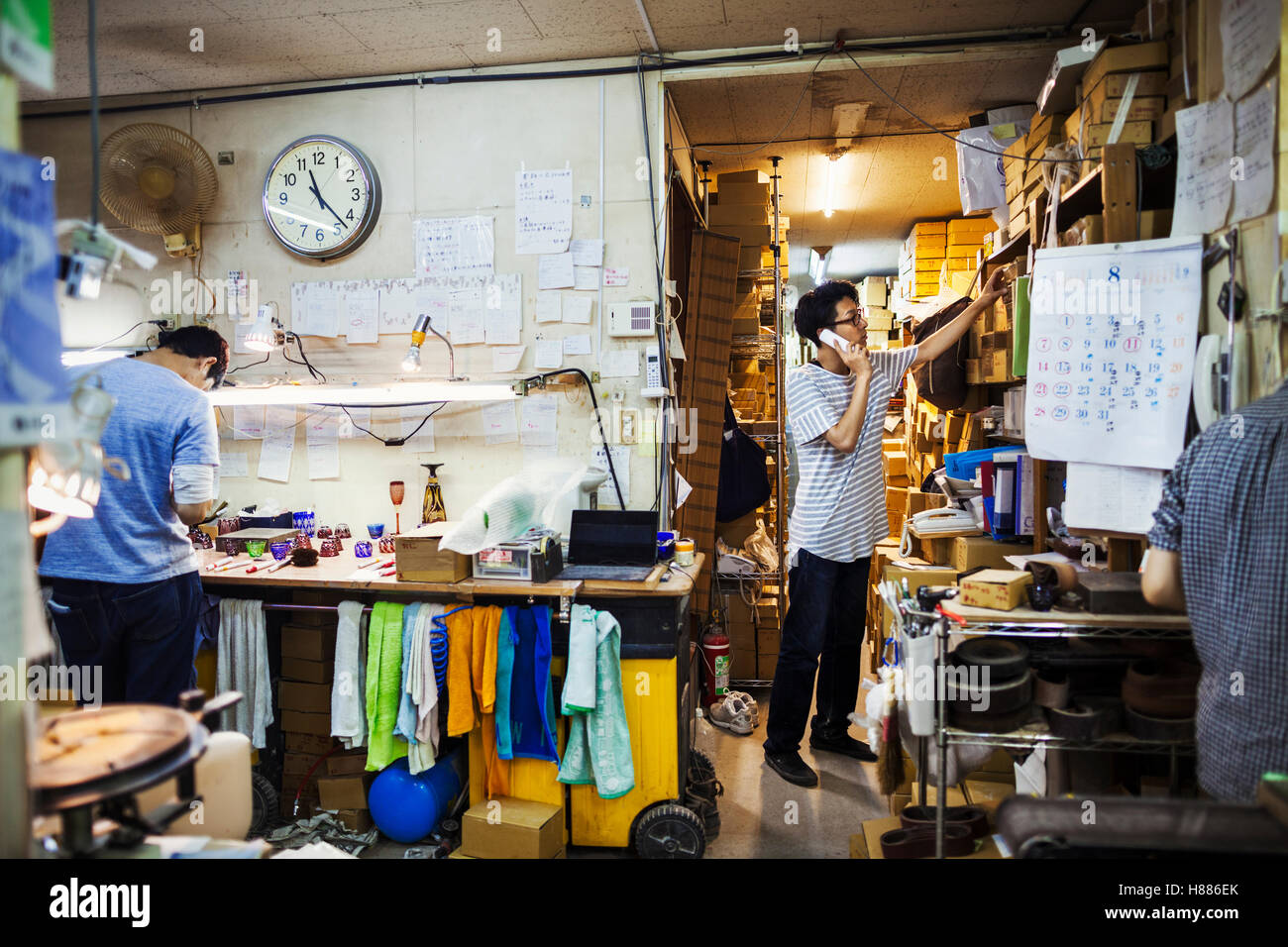 Due persone al lavoro in un produttore di vetro del workshop e per l'ufficio, uno sul telefono. Foto Stock