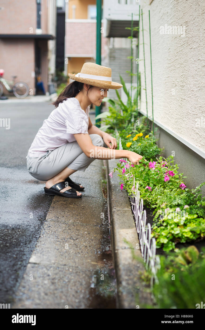 Casa di famiglia. Una donna accovacciata e piantare fiori in una piccola striscia di terreno. Foto Stock
