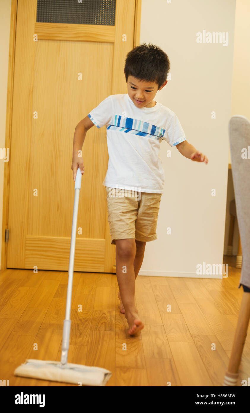 Casa di famiglia. Un ragazzo con un mop la pulizia di un pavimento in legno. Facendo la sua quota di pulizia della casa. Foto Stock