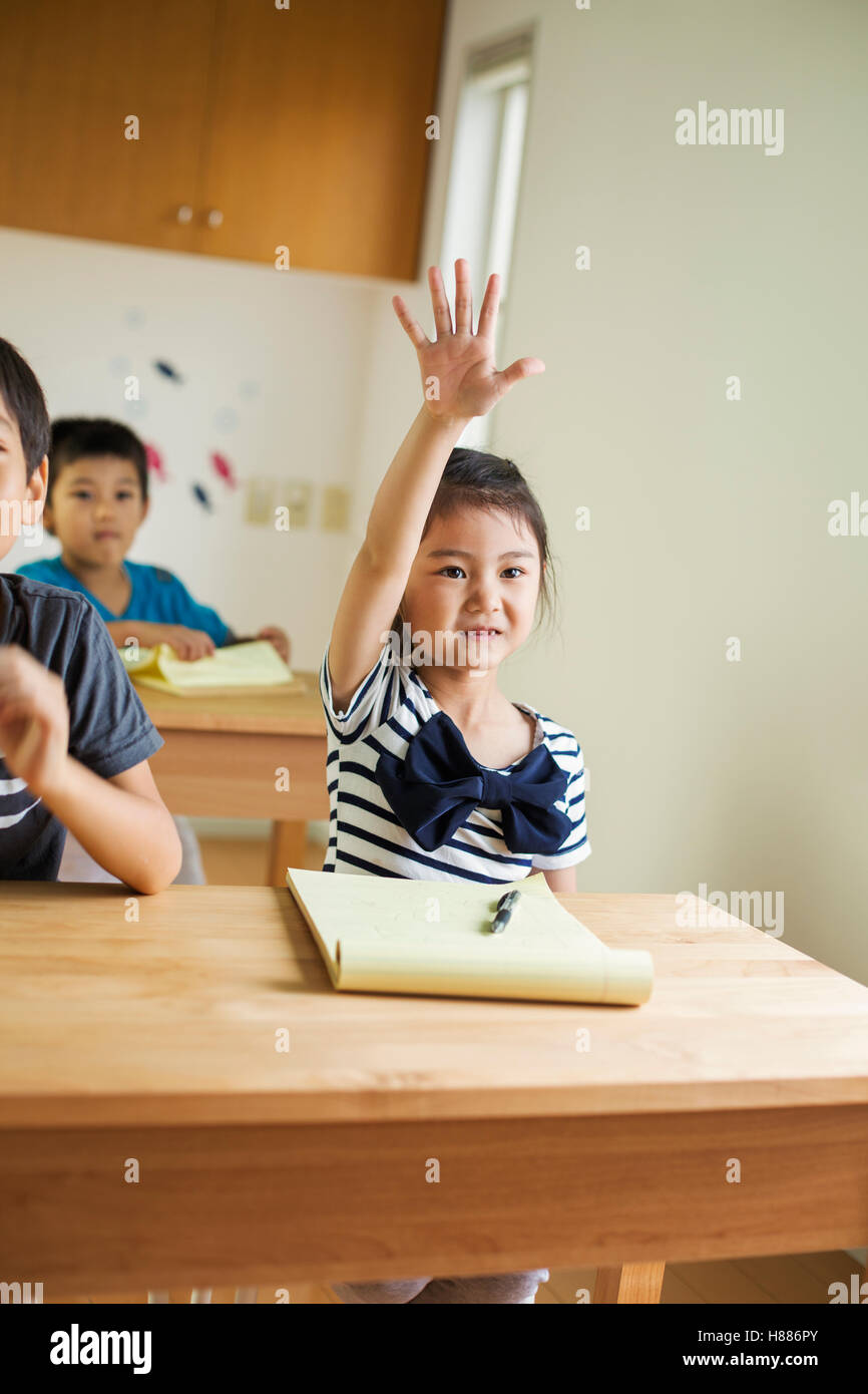 Un gruppo di bambini in una classe, uno con la sua mano pronto a rispondere a una domanda. Foto Stock