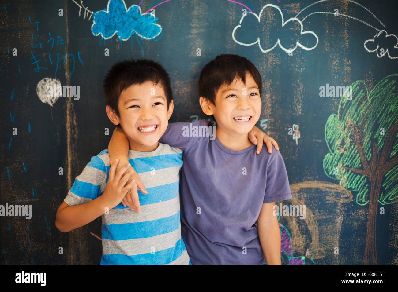 I bambini a scuola. Due ragazzi in piedi con le braccia intorno a ogni altro spalle da una lavagna. Divertirsi a scuola. Foto Stock