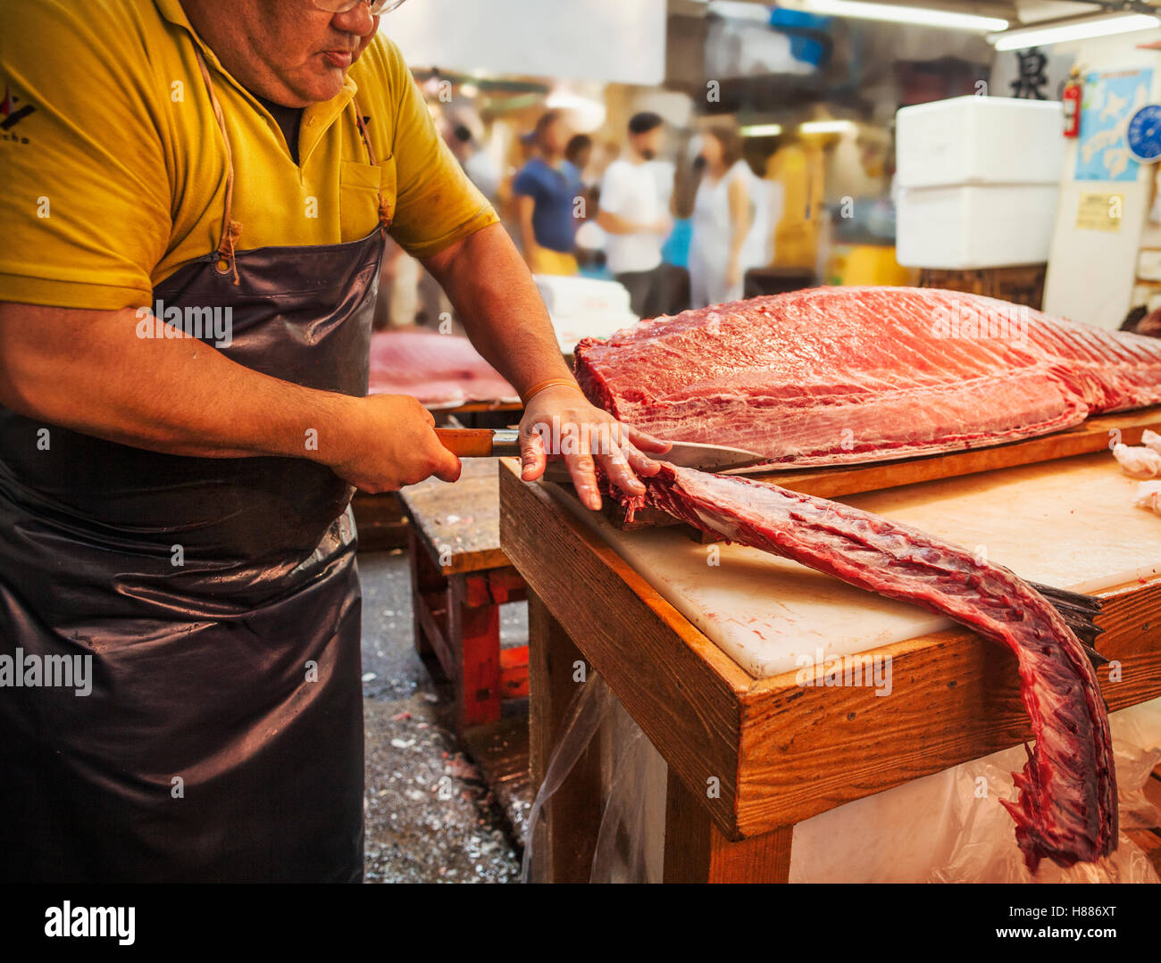 Un tradizionale mercato del pesce fresco in Tokyo. Un pescivendolo lavora la sfilettatura un grande pesce su una lastra. Persone in background. Foto Stock