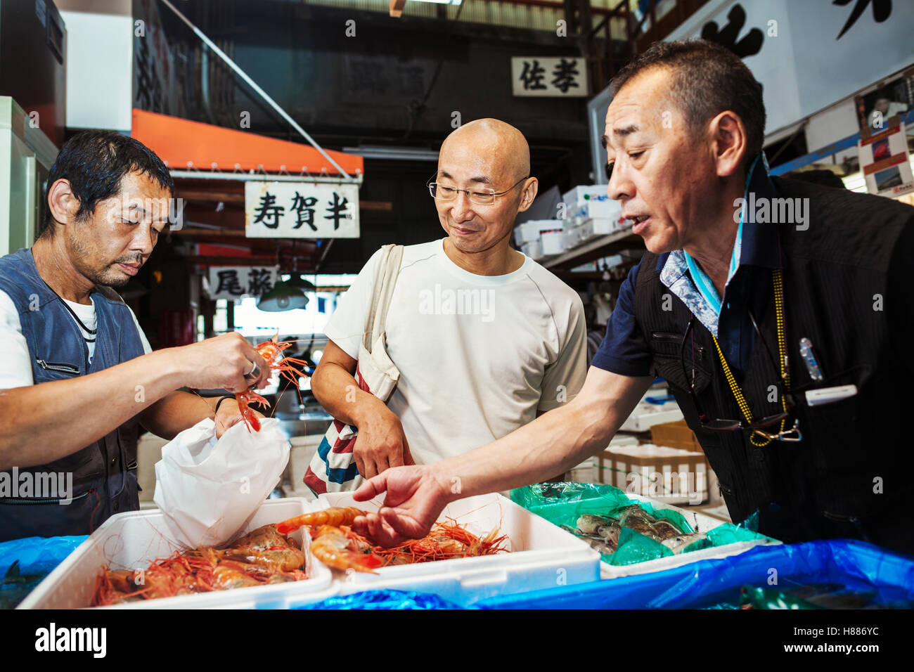 Mercato del pesce fresco in Tokyo. Due persone selezionando i crostacei per un cliente a comprare, riempimento di un sacco da box di gamberi. Foto Stock