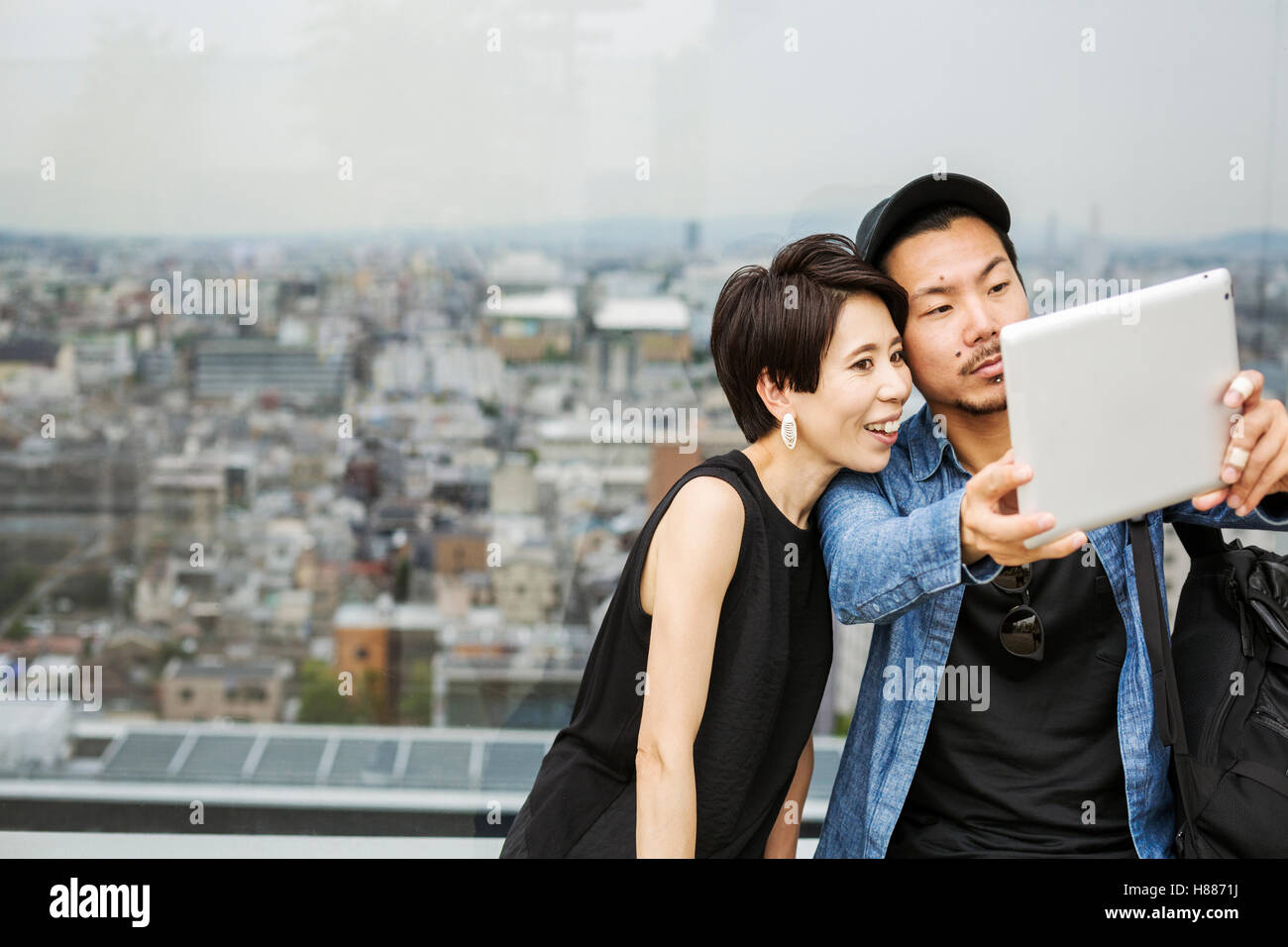 Due persone, l uomo e la donna prendendo un selfie con una tavoletta digitale, di fronte a una vista su di una grande città. Foto Stock