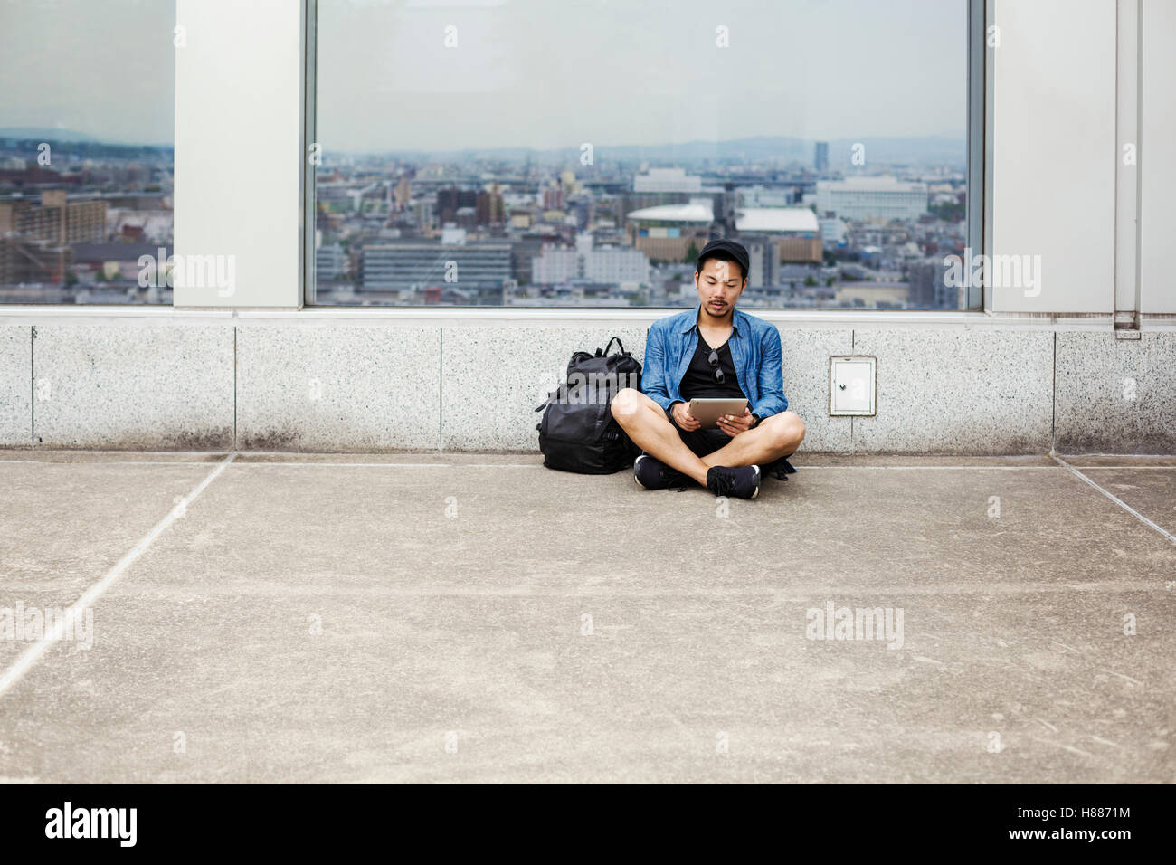 Un uomo seduto sul pavimento usando il suo smart phone, di fronte a un punto di visualizzazione finestra sulla città. Foto Stock